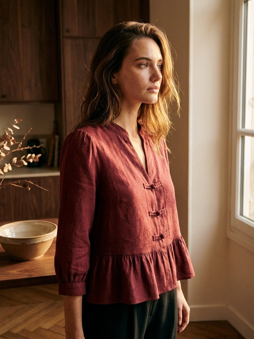 Mujer con la blusa Emilie burdeos de Ycoo con alamares, de perfil junto a una ventana